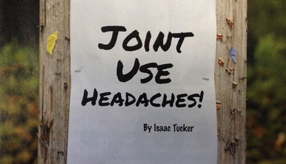 Paper with words "Joint Use Headaches! by Isaac Tucker" tacked to utility pole 
