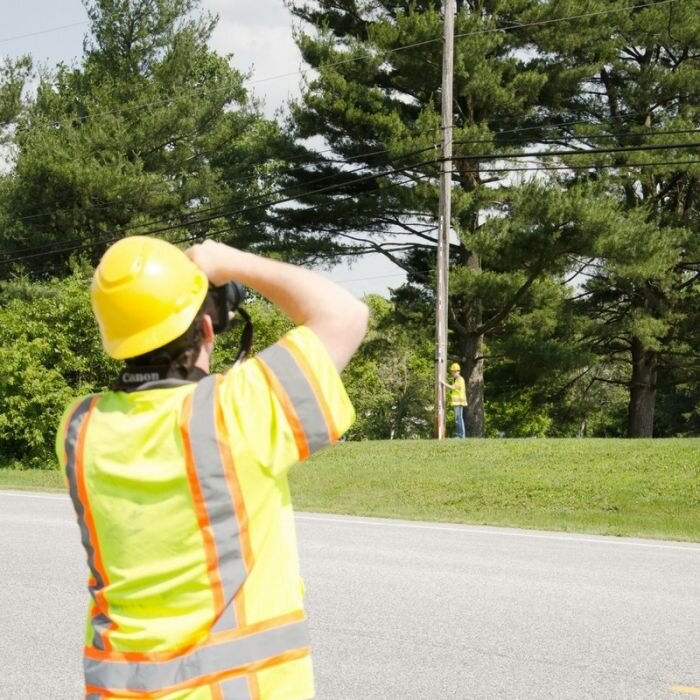Two field crew members in reflective gear gather data of poles. 